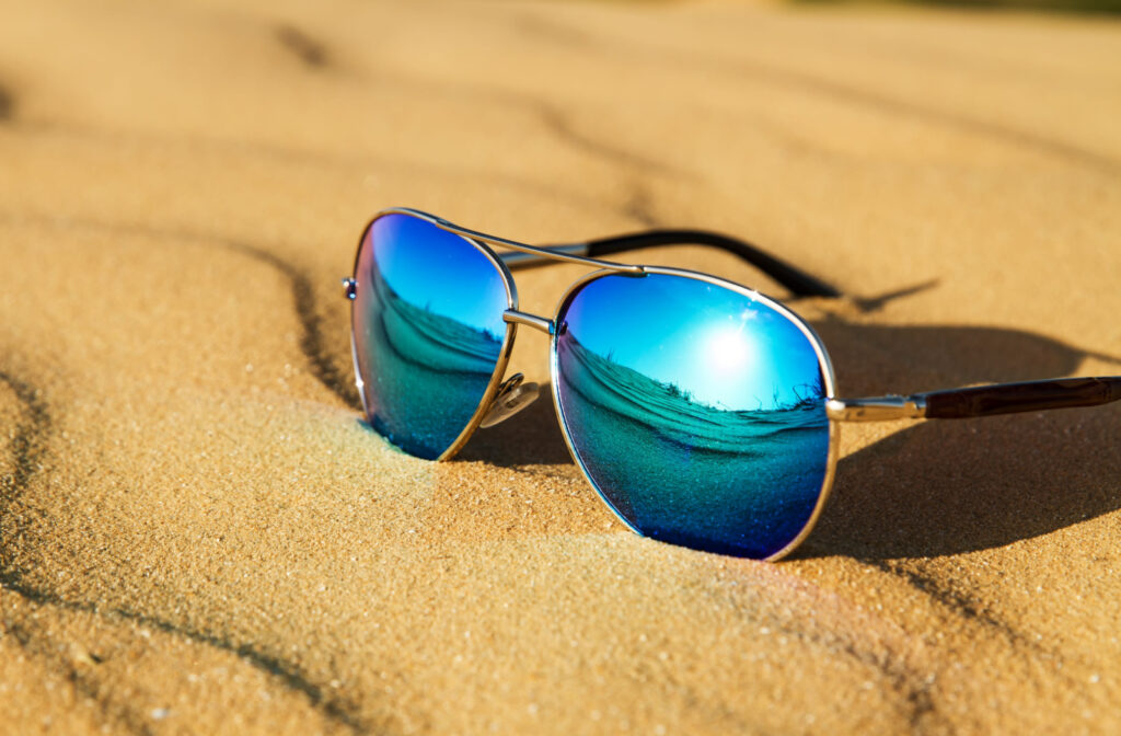 A pair of polarized sunglasses on sand reflecting the sunlight.