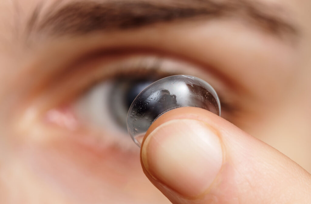 A close-up of a scleral contact lens delicately rests on the tip of a finger, aiming to insert it onto the eye with precision.
