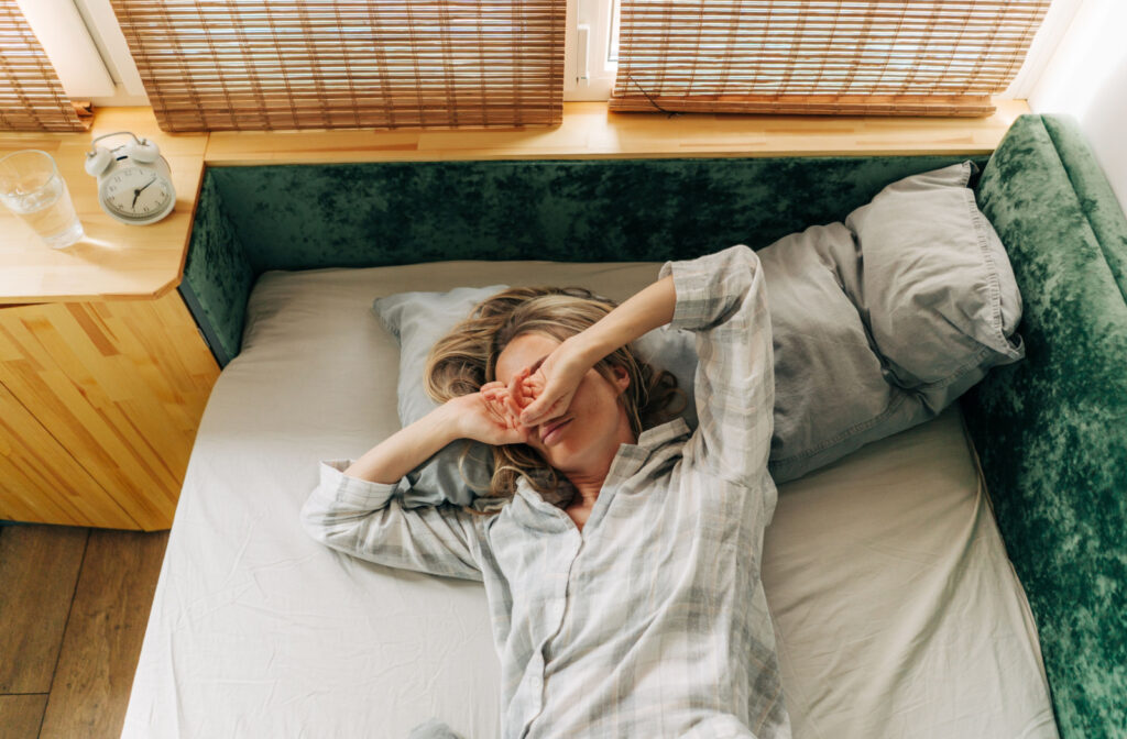 A woman in her sleep wear rubbing her eyes possibly because of morning eye dryness.