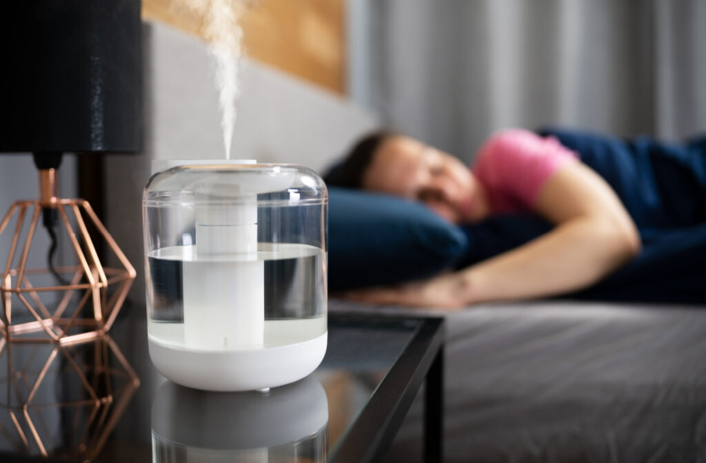 A white humidifier on a bed side table next to a sleeping woman.